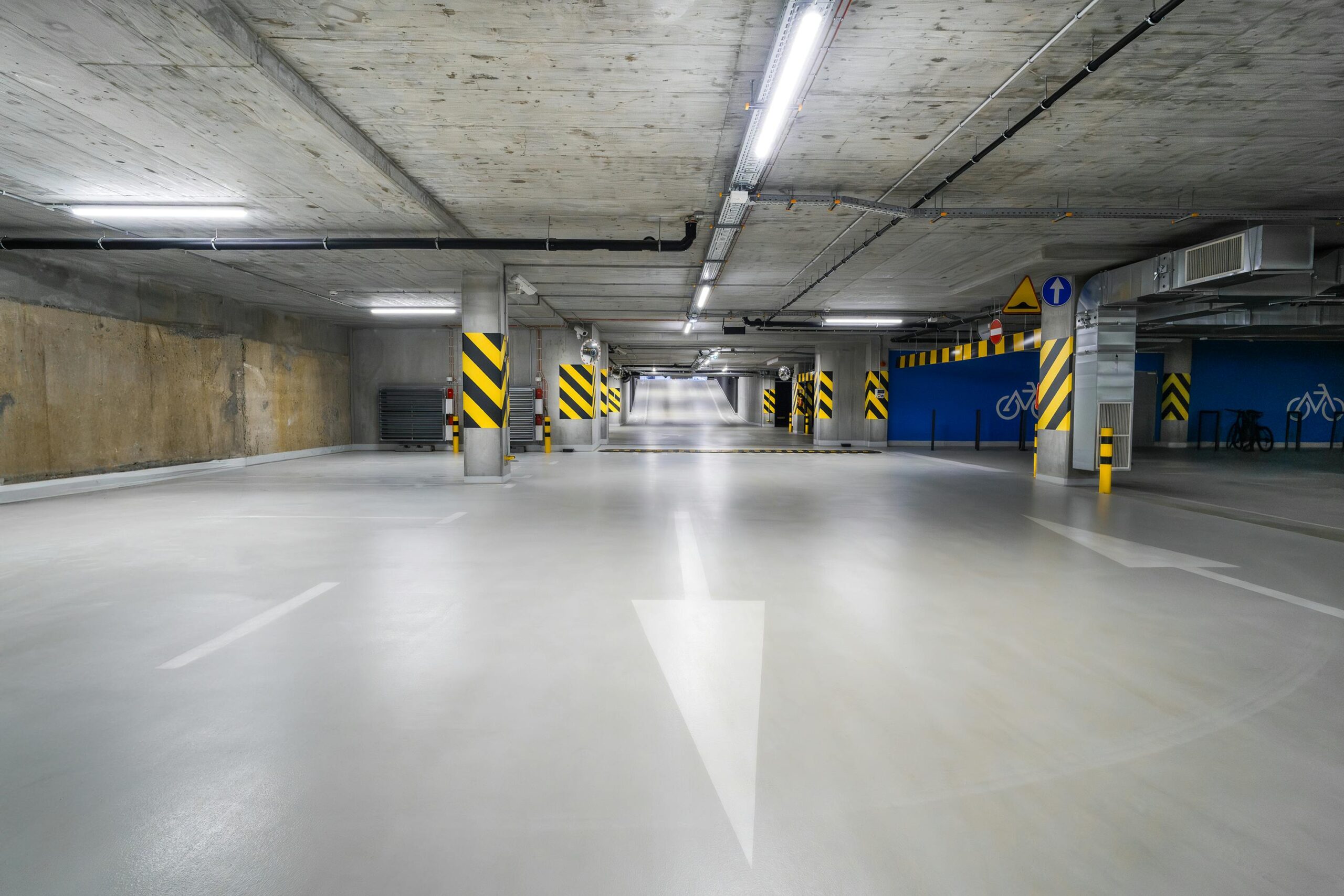 Explore the modern, well-lit, and spacious underground parking garage in Poznań with clear directional signs.